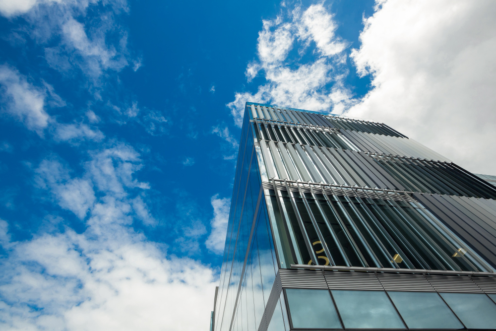 Modern glass building with vertical sunshades set against a vibrant blue sky with scattered white clouds.
